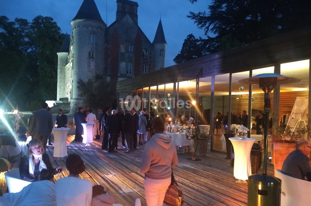 Groupe de personnes réunies en soirée sur une terrasse éclairée, avec un château en arrière-plan.