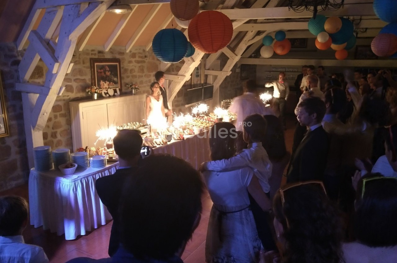 Des invités regardent un couple devant une table illuminée de bougies dans une salle décorée de lanternes colorées.