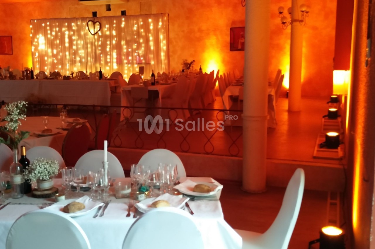 Salle de réception décorée avec des guirlandes lumineuses, tables dressées et ambiance chaleureuse.