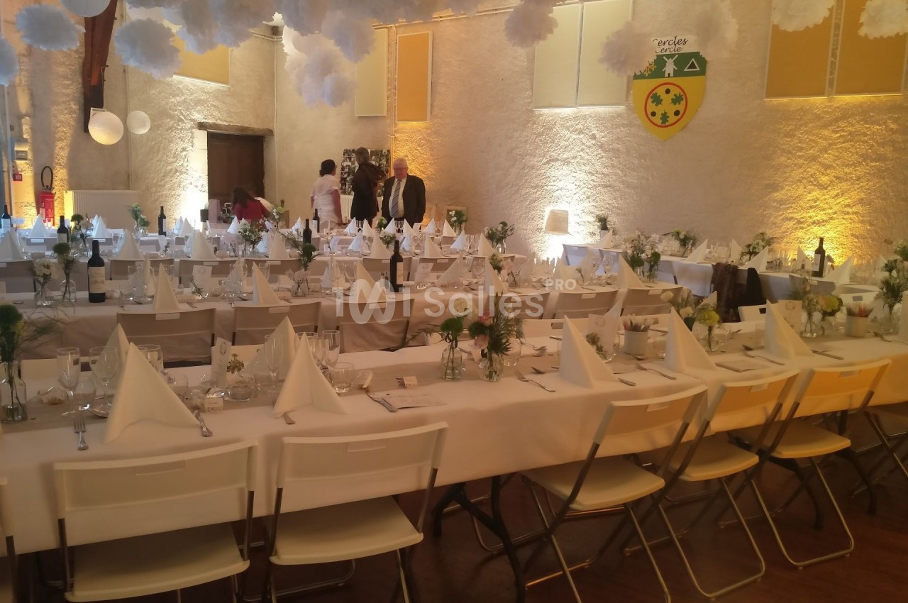 Salle de réception décorée avec des tables dressées, nappes blanches, serviettes pliées et arrangements floraux.