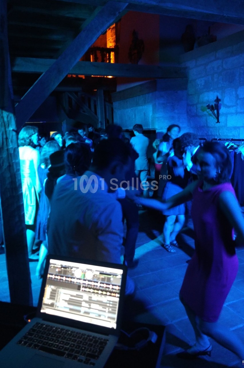 Personnes dansant dans une salle éclairée par des lumières bleues, avec un ordinateur de DJ au premier plan.