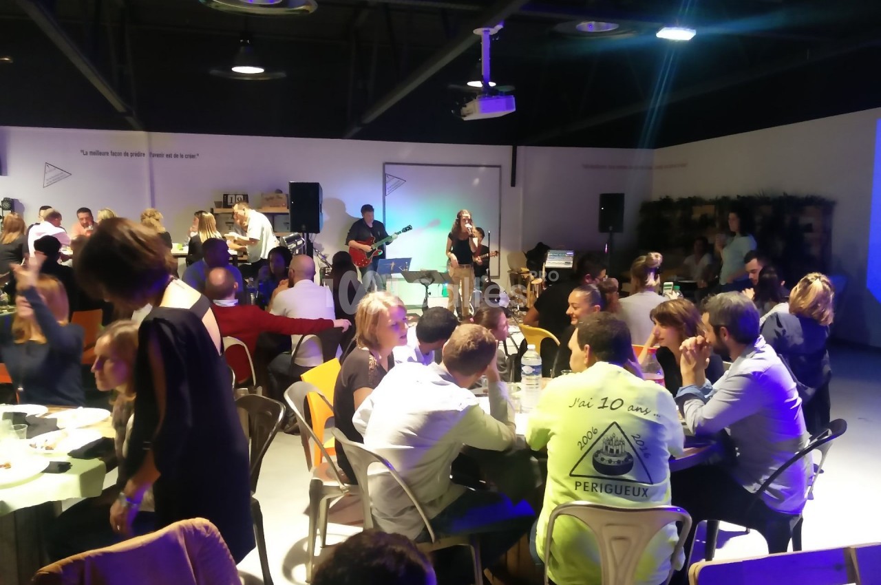 Des personnes dînent et discutent dans une salle animée avec un groupe de musique jouant en arrière-plan.