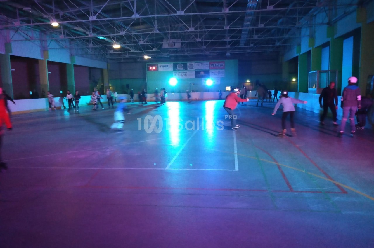 Personnes patinant dans une patinoire intérieure éclairée par des lumières colorées dans une ambiance nocturne.