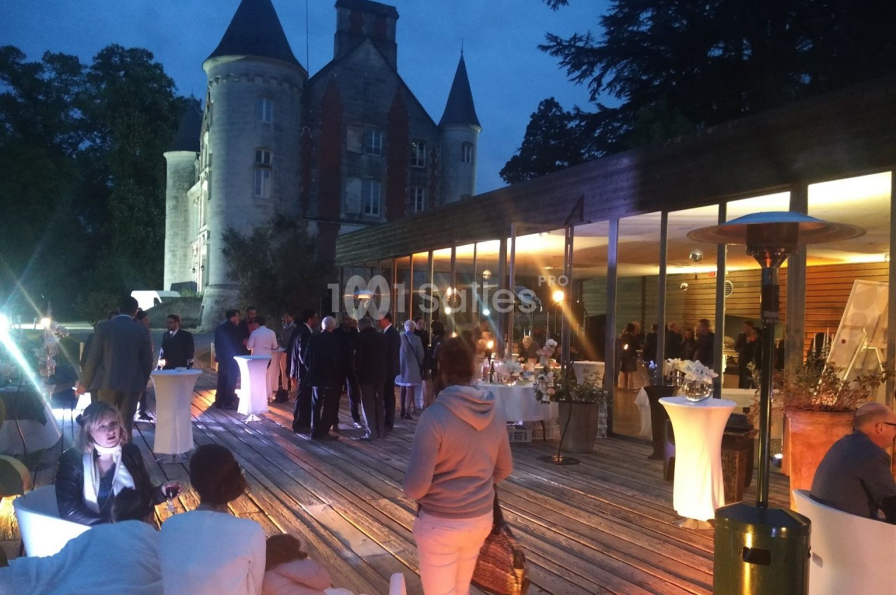 Groupe de personnes réunies en soirée sur une terrasse éclairée, avec un château en arrière-plan.