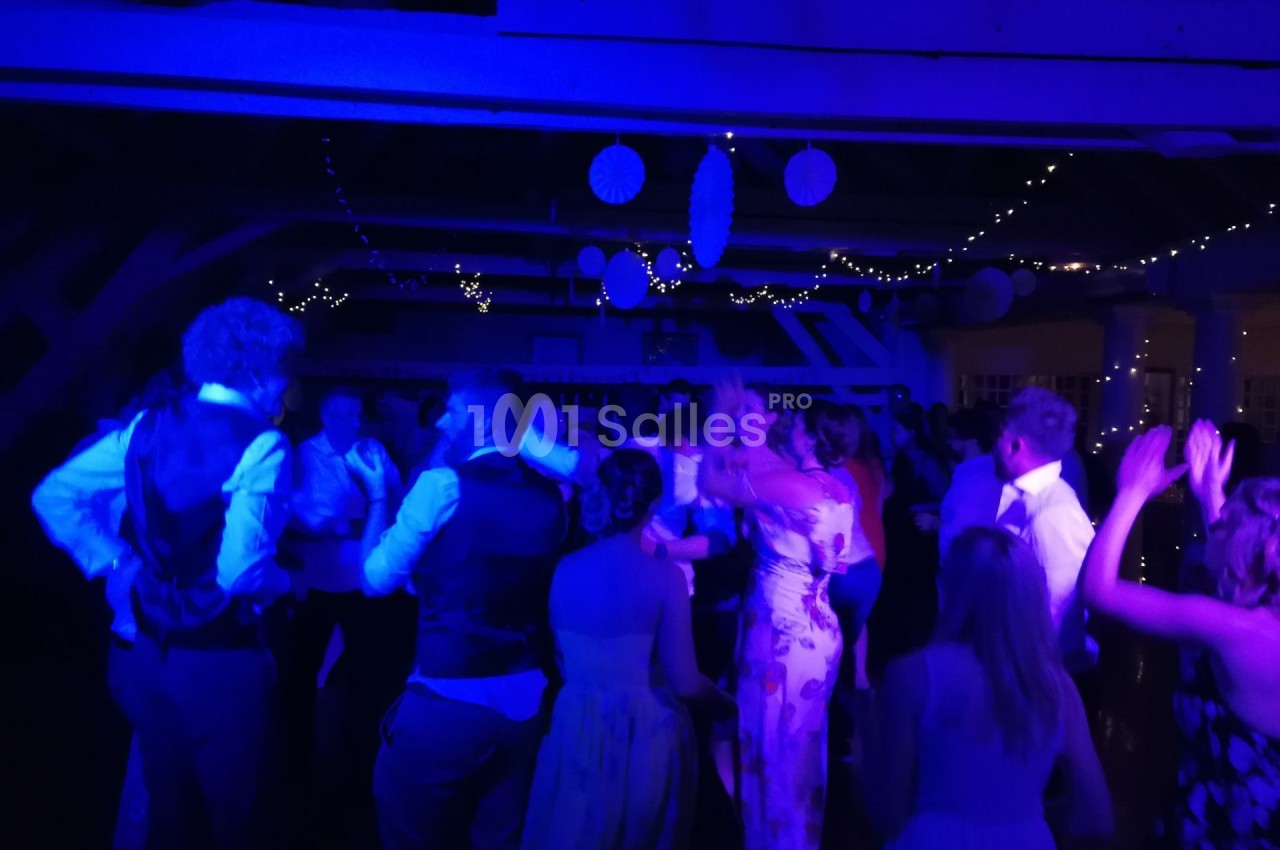 Groupe de personnes dansant sous des lumières bleues dans une salle décorée avec des guirlandes lumineuses et des…