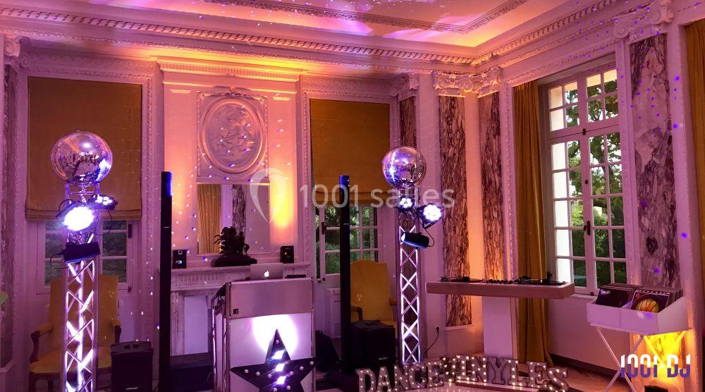 Salle élégante avec décoration lumineuse, projecteurs colorés, boules à facettes et équipement de DJ installé.