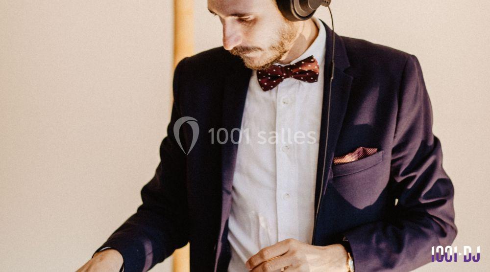 Un homme en costume avec un nœud papillon mixe de la musique avec un casque audio.