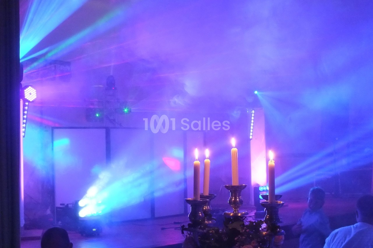 Salle de fête avec éclairages colorés, fumée et chandeliers allumés au premier plan.