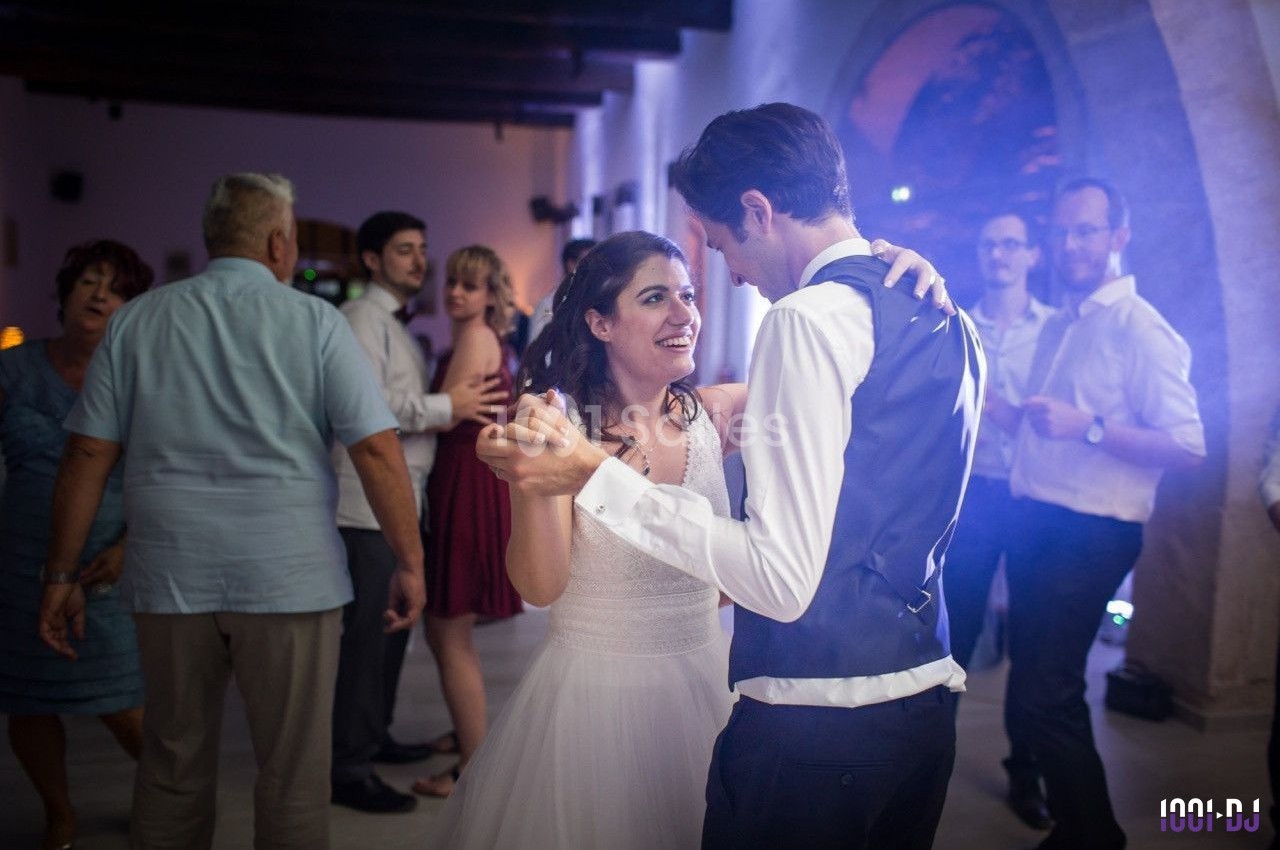 Un couple danse lors d'une fête dans une salle éclairée, entouré de plusieurs invités.