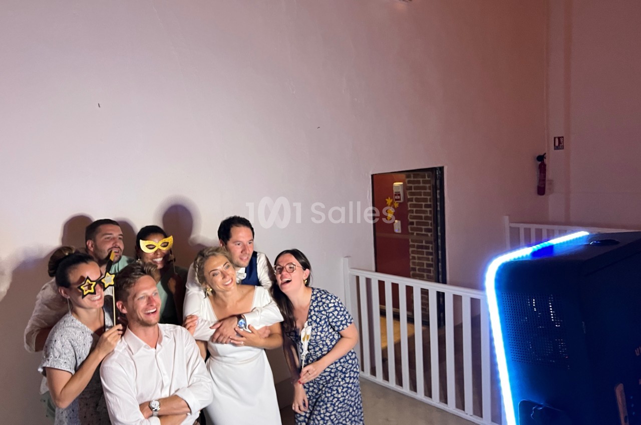 Un groupe de personnes souriantes pose avec des accessoires ludiques devant une borne photo dans une salle éclairée.