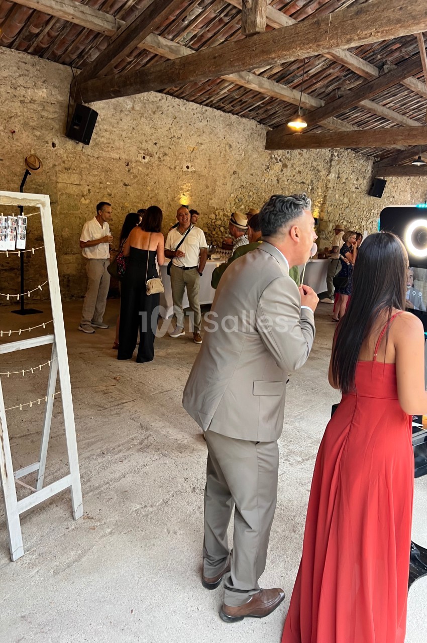 Des personnes discutent et utilisent une borne photo dans une salle en pierre avec un plafond en bois.