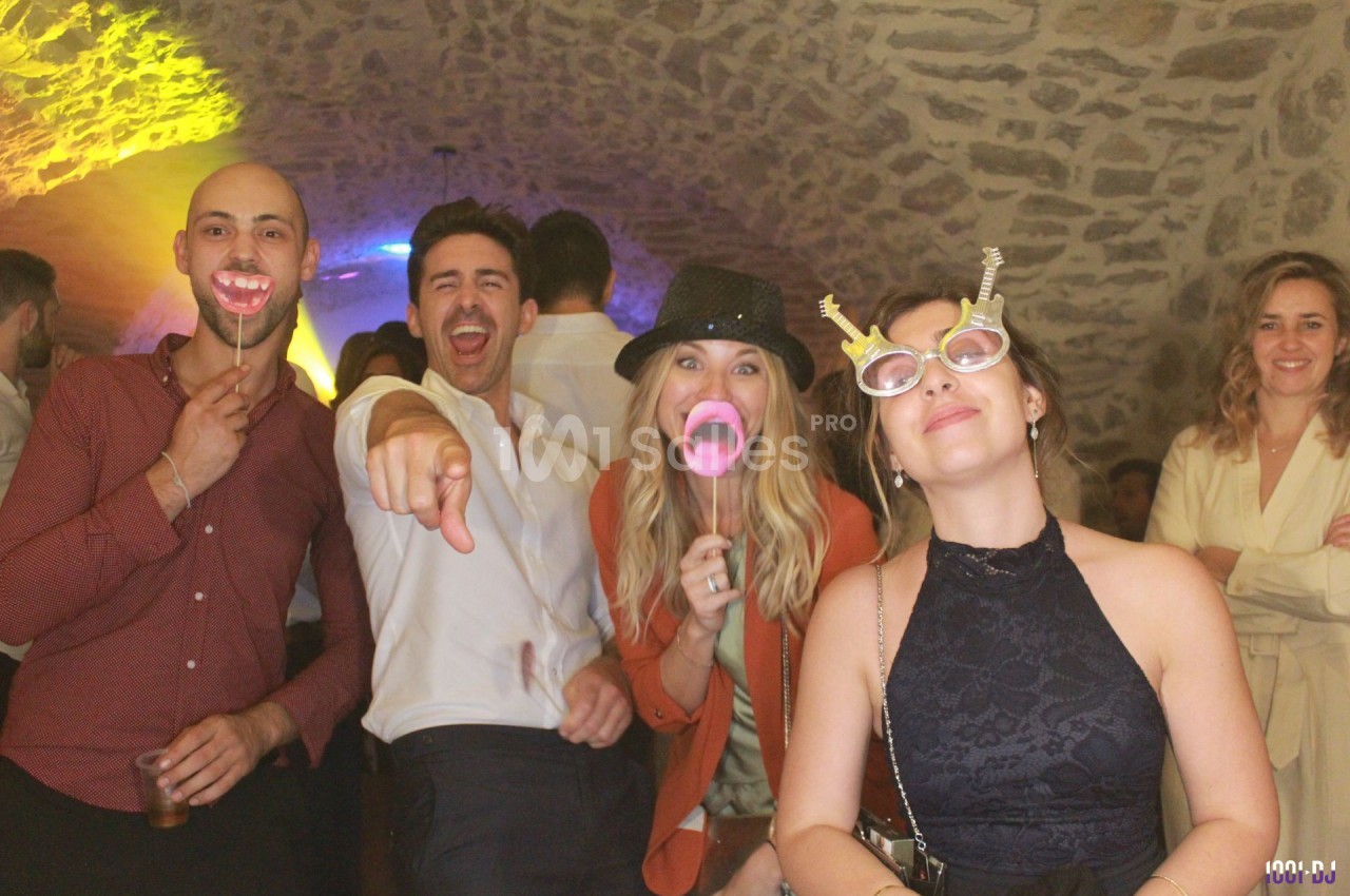 Des personnes souriantes posent avec des accessoires festifs dans une ambiance conviviale sous une voûte en pierre.