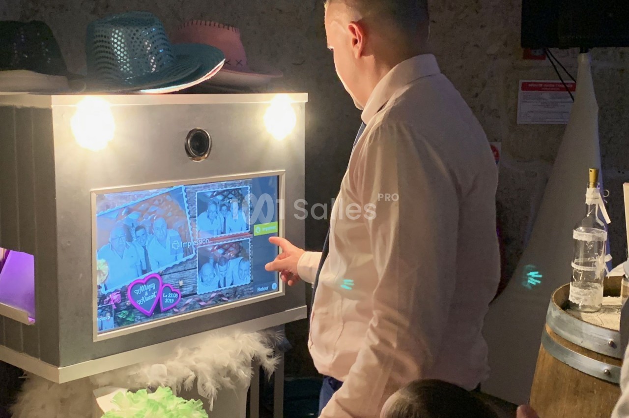 Un homme utilise une borne photo interactive lors d'un événement, entouré d'accessoires festifs.