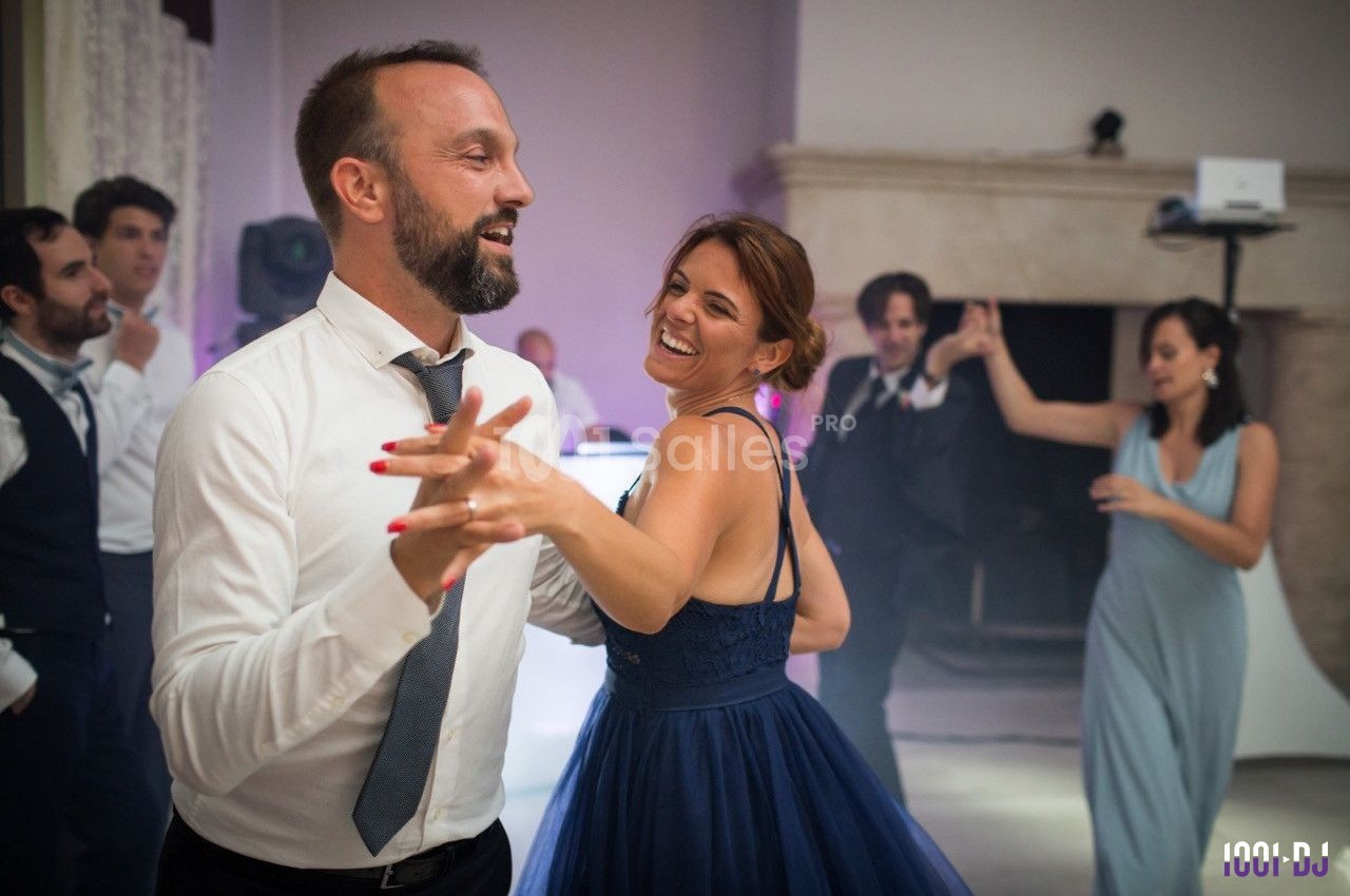 Un couple danse joyeusement lors d'une soirée, entouré d'autres invités en tenue élégante.