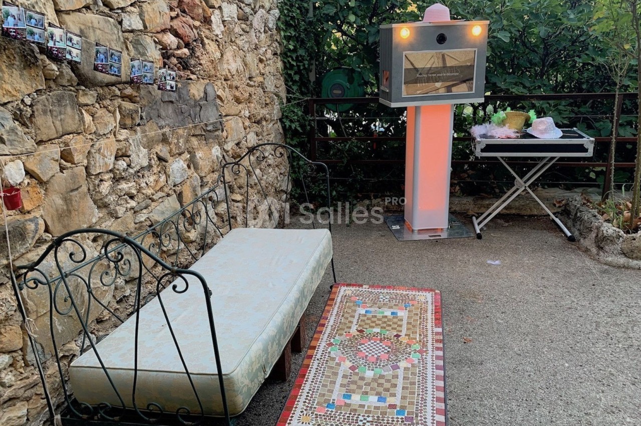Canapé en fer forgé, table basse ornée de mosaïques et four à pizza dans une cour extérieure en pierre.