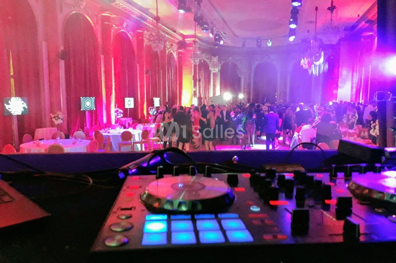 Vue d'une salle de réception illuminée avec des invités, prise depuis une table de mixage en premier plan.