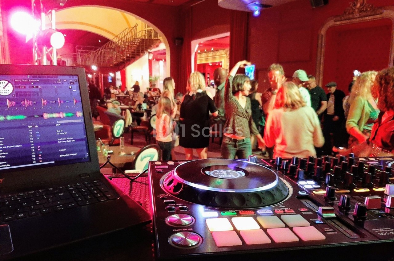 Vue d'une piste de danse animée dans une salle, avec une table de mixage et un ordinateur au premier plan.