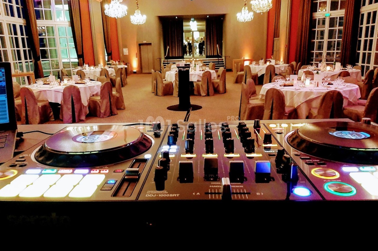 Console de DJ allumée au premier plan, avec une salle de réception élégamment décorée en arrière-plan.