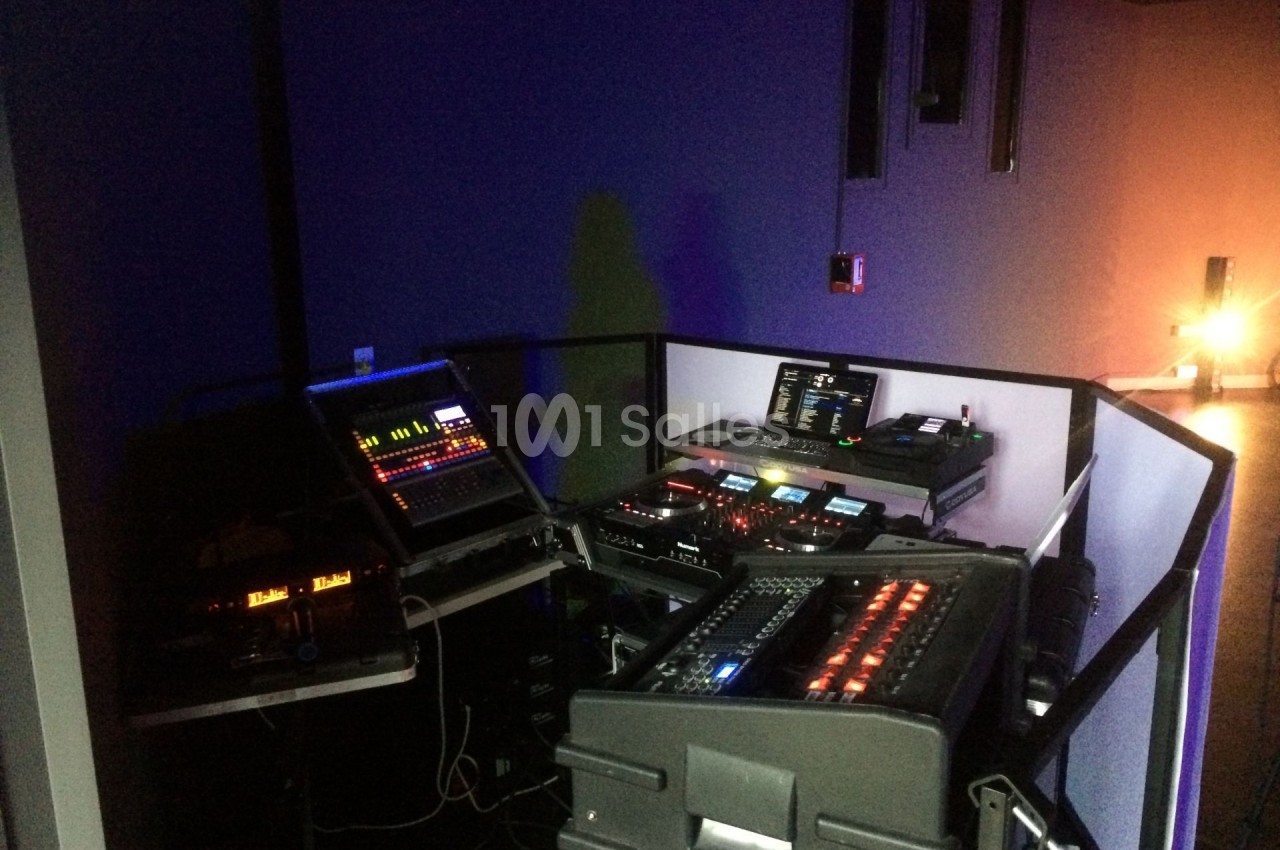 Poste de contrôle audio et lumière dans une salle sombre, équipé de consoles, écrans et matériel technique.