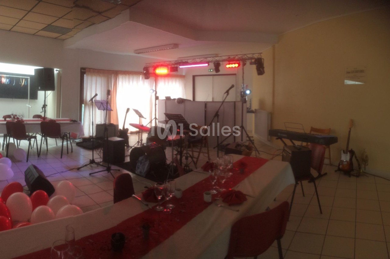 Salle décorée avec des tables dressées, des ballons et une scène équipée d'instruments de musique et de projecteurs.