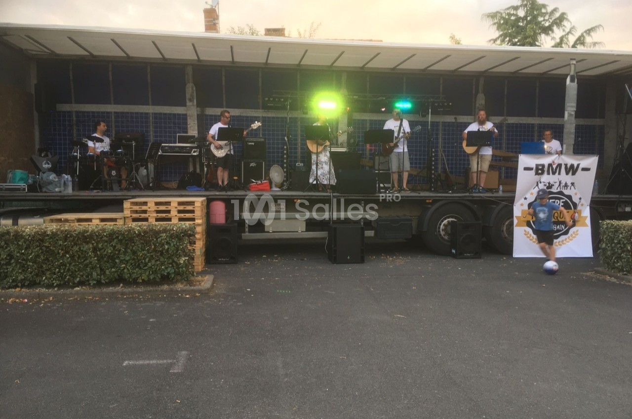 Un groupe de musiciens joue sur une scène extérieure équipée de lumières et d'instruments, devant un public absent.