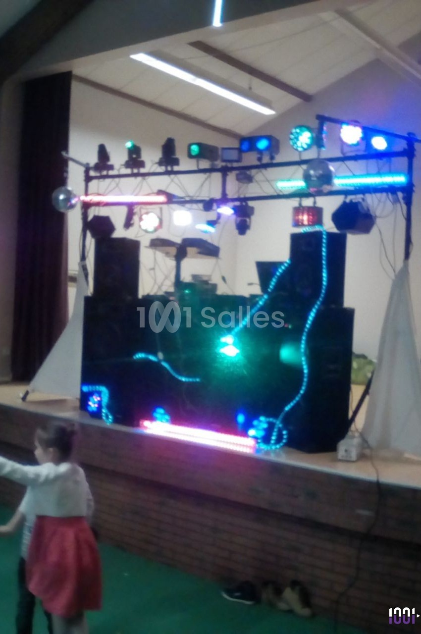 Installation de matériel de sonorisation et d'éclairage coloré sur une scène intérieure, avec des enfants au premier plan.