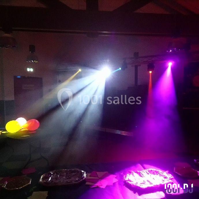 Jeux de lumière colorés dans une salle sombre avec des ballons et des tables décorées pour un événement festif.