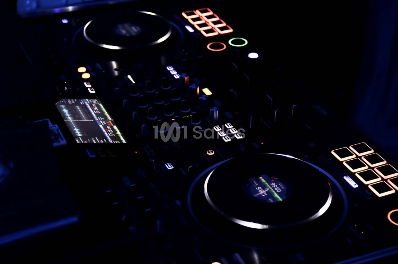 Console de mixage DJ éclairée dans un environnement sombre, avec boutons et écrans lumineux.