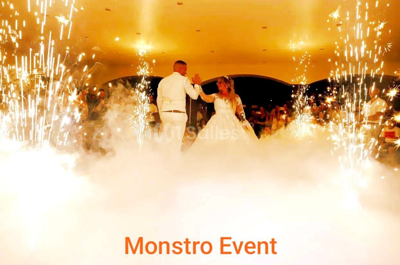 Un couple danse au centre d'une salle entourée d'effets pyrotechniques et de fumée blanche.