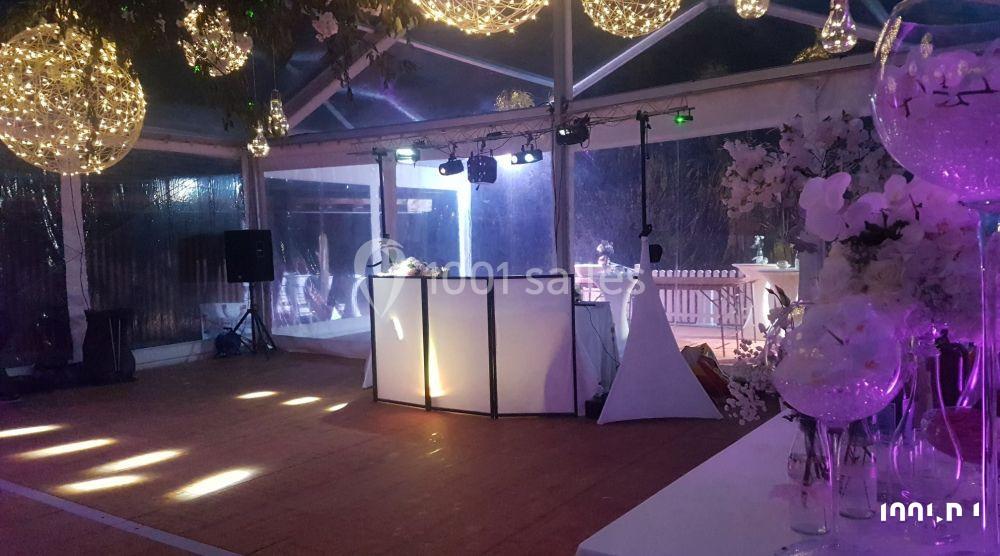 Salle de réception décorée avec des guirlandes lumineuses suspendues, une piste de danse et un espace DJ éclairé.