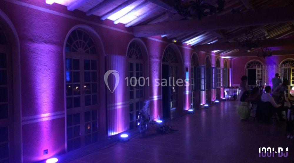 Salle avec murs roses, éclairée par des lumières violettes et blanches, avec des arches vitrées et un plafond en bois.