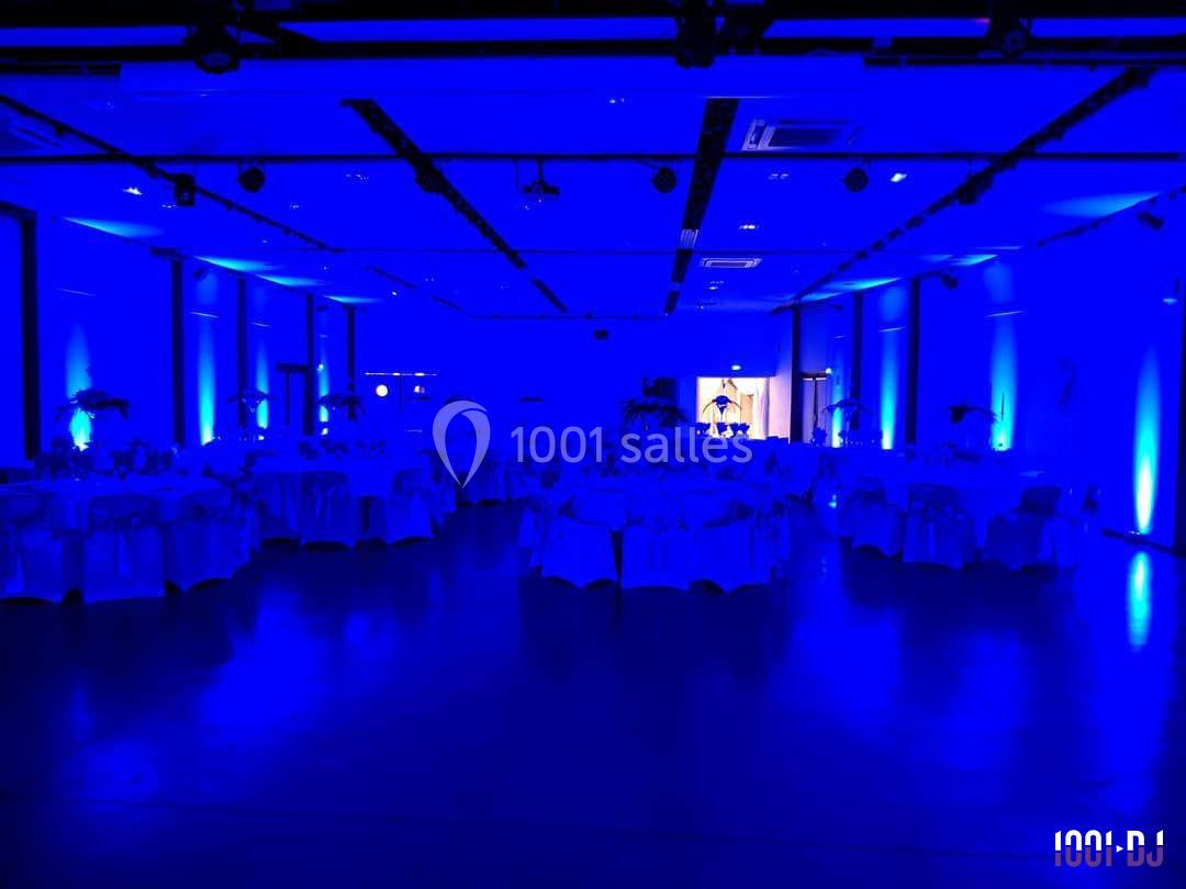 Salle de réception éclairée en bleu avec des tables rondes dressées pour un événement.