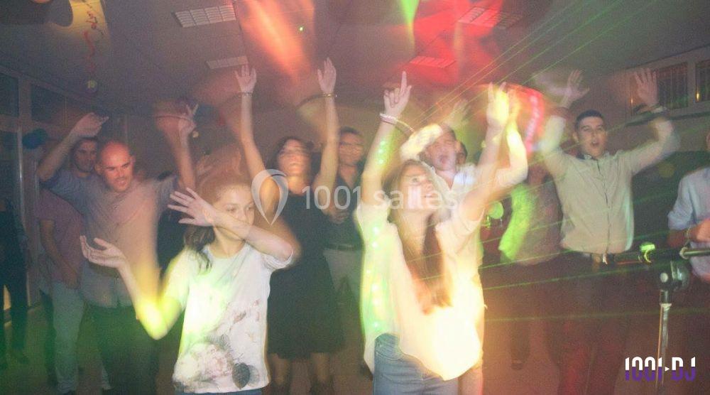 Des personnes dansent dans une ambiance festive avec des lumières colorées dans une salle sombre.