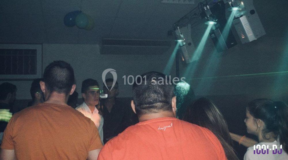 Groupe de personnes dans une salle sombre éclairée par des projecteurs, ambiance de fête ou de soirée.