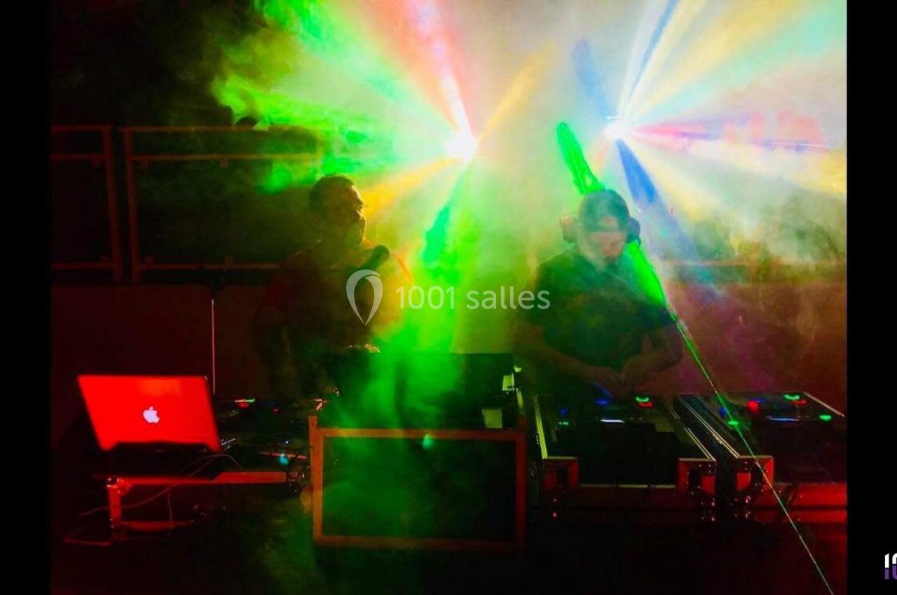 Deux DJ mixant sur scène avec des jeux de lumière colorés et une ambiance enfumée.