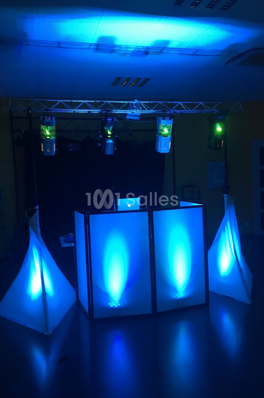 Installation de DJ avec éclairage bleu, comprenant une table de mixage et des spots lumineux dans une salle sombre.
