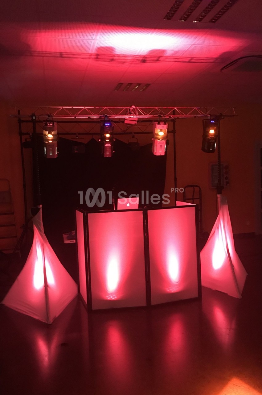 Pupitre de DJ éclairé par des lumières rouges et oranges, avec des structures lumineuses triangulaires autour.