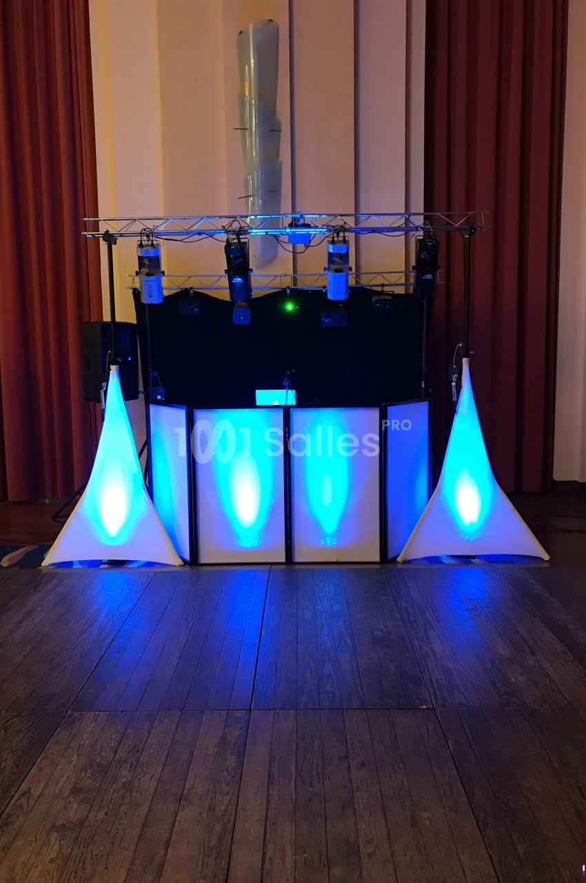 Équipement de sonorisation et éclairage avec lumières bleues installé dans une salle avec rideaux rouges.