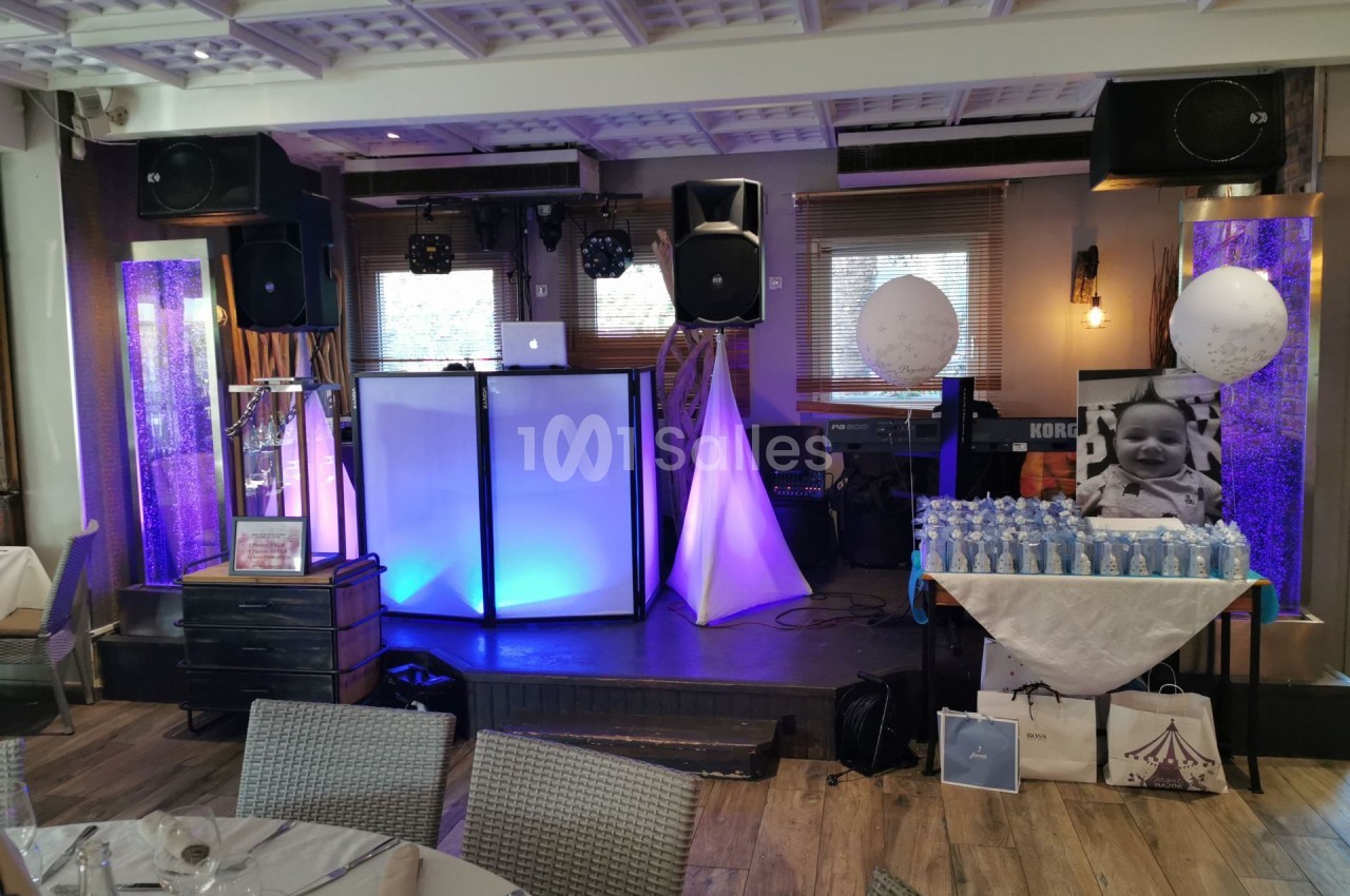 Salle décorée pour un événement avec une table de boissons, un stand DJ éclairé et des ballons décoratifs.