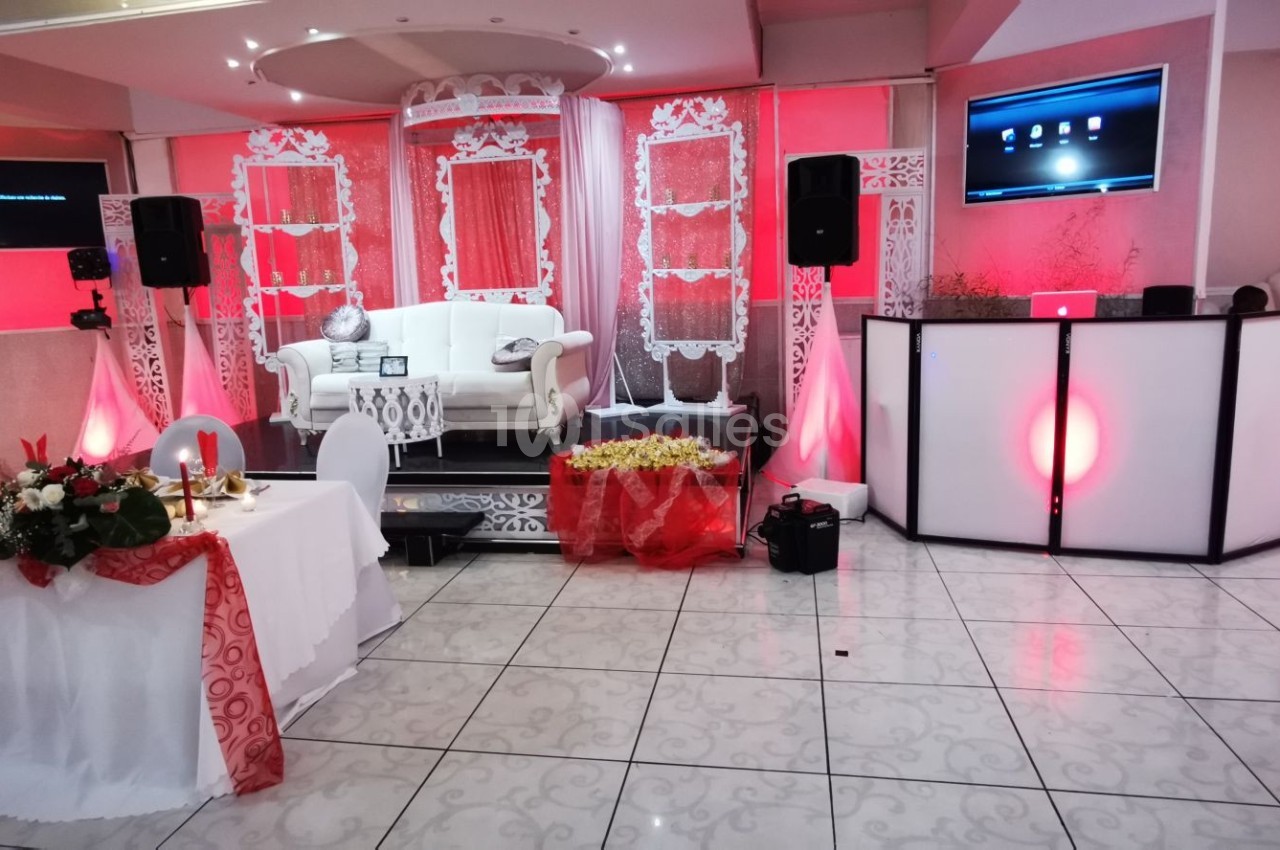 Salle de réception décorée en rouge et blanc avec une estrade, un canapé, une table ornée et un espace DJ.