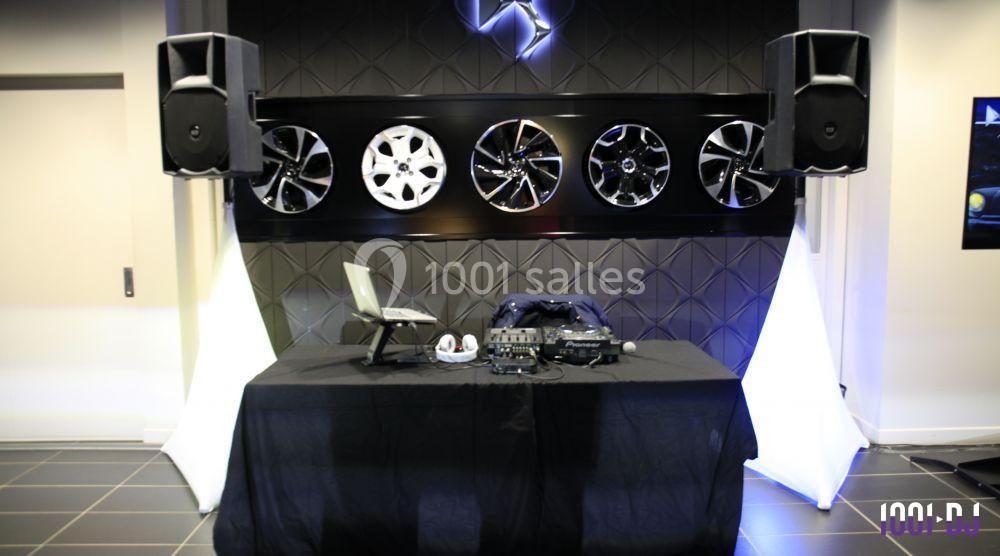 Table de DJ équipée d'un ordinateur portable, casque et contrôleur, devant un mur décoré de jantes de voiture.