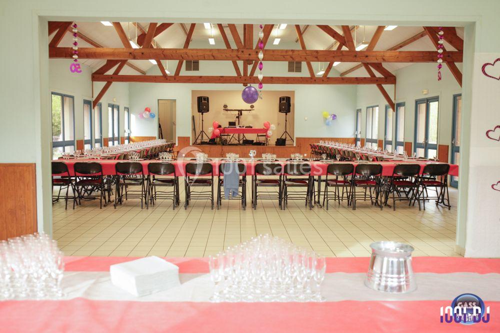 Grande salle décorée pour un événement, avec tables alignées, nappes rouges et blanches, et ballons suspendus.