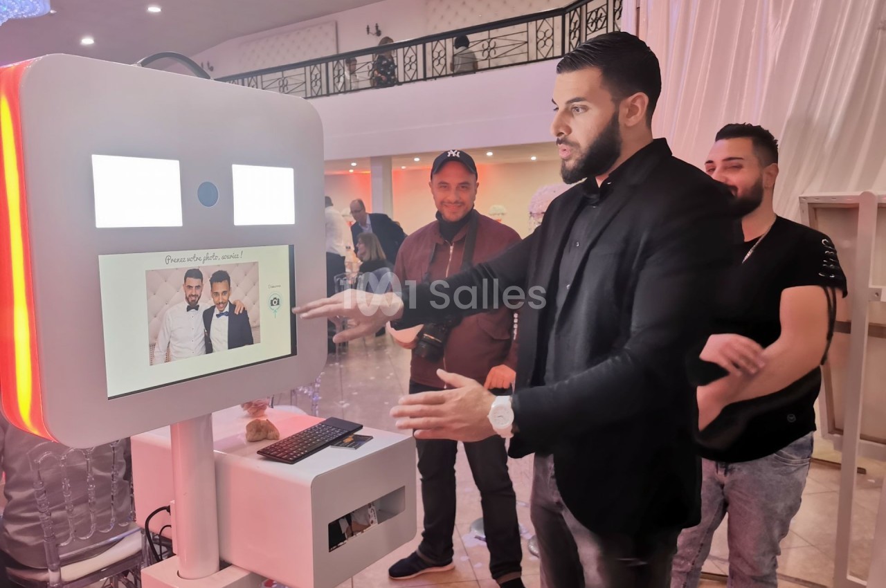 Un homme interagit avec une borne photo dans un espace intérieur lumineux, entouré de plusieurs personnes.