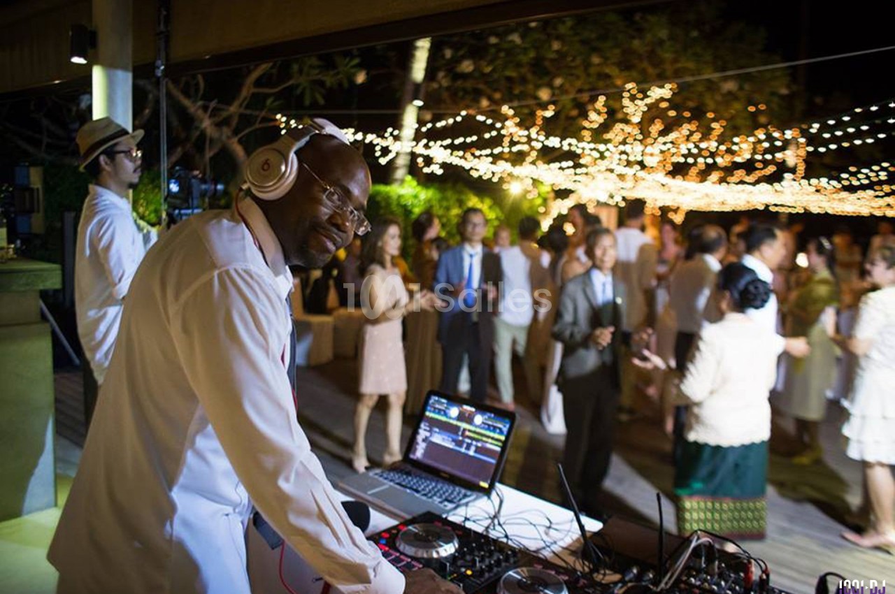 Un DJ mixe de la musique lors d'une soirée en plein air avec des invités dansant sous des guirlandes lumineuses.