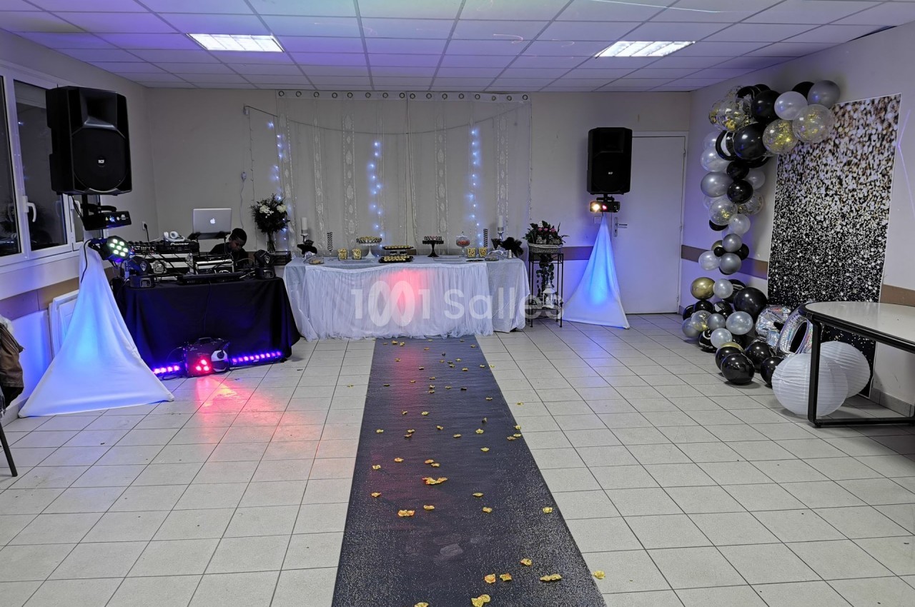 Salle décorée pour un événement avec table de buffet, éclairages, piste ornée de pétales et ballons festifs.