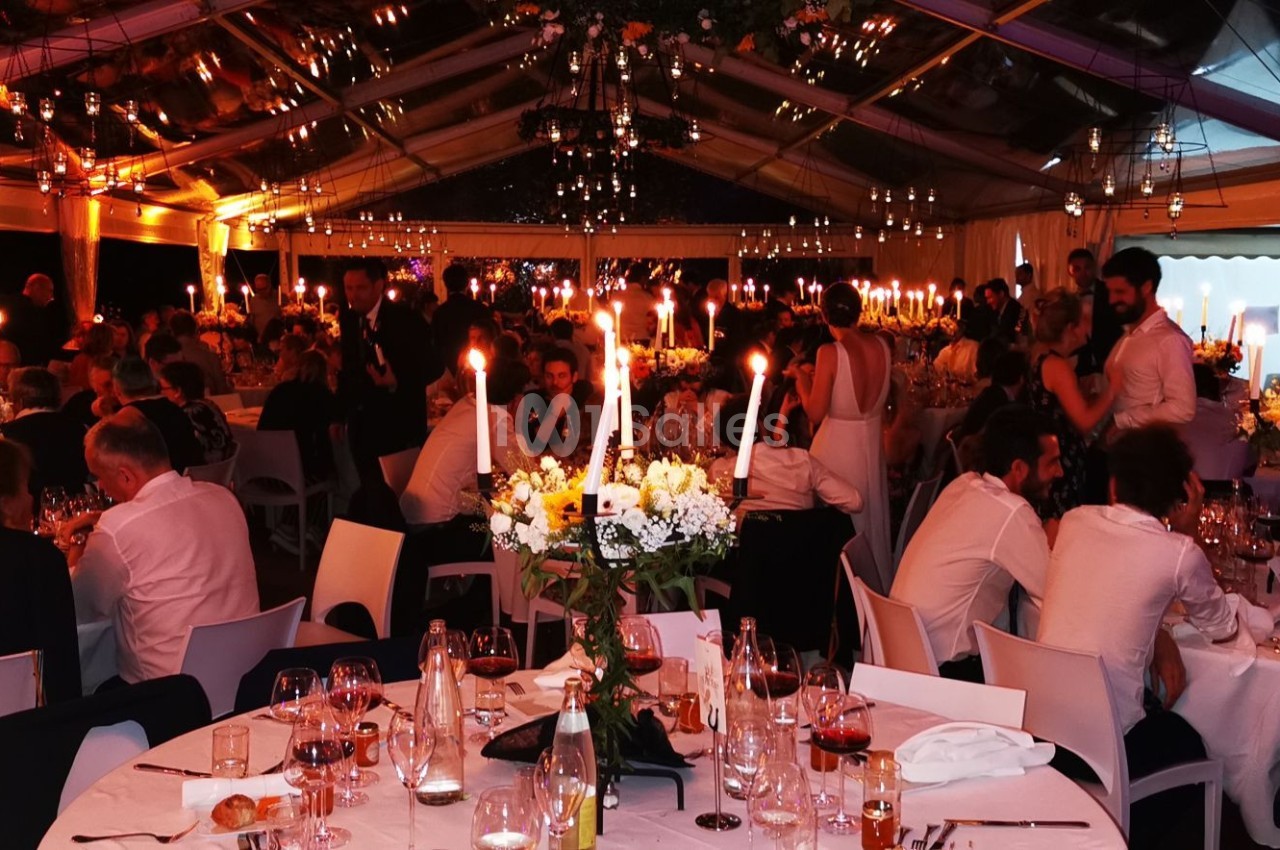 Salle de réception illuminée avec des invités attablés, décorations florales et chandeliers sur les tables.