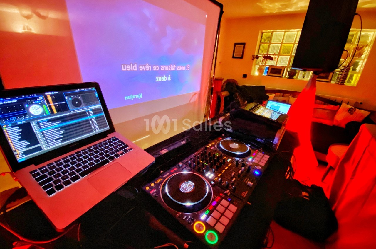 Poste de DJ avec ordinateur portable et platines, installé dans une pièce éclairée par des lumières rouges.