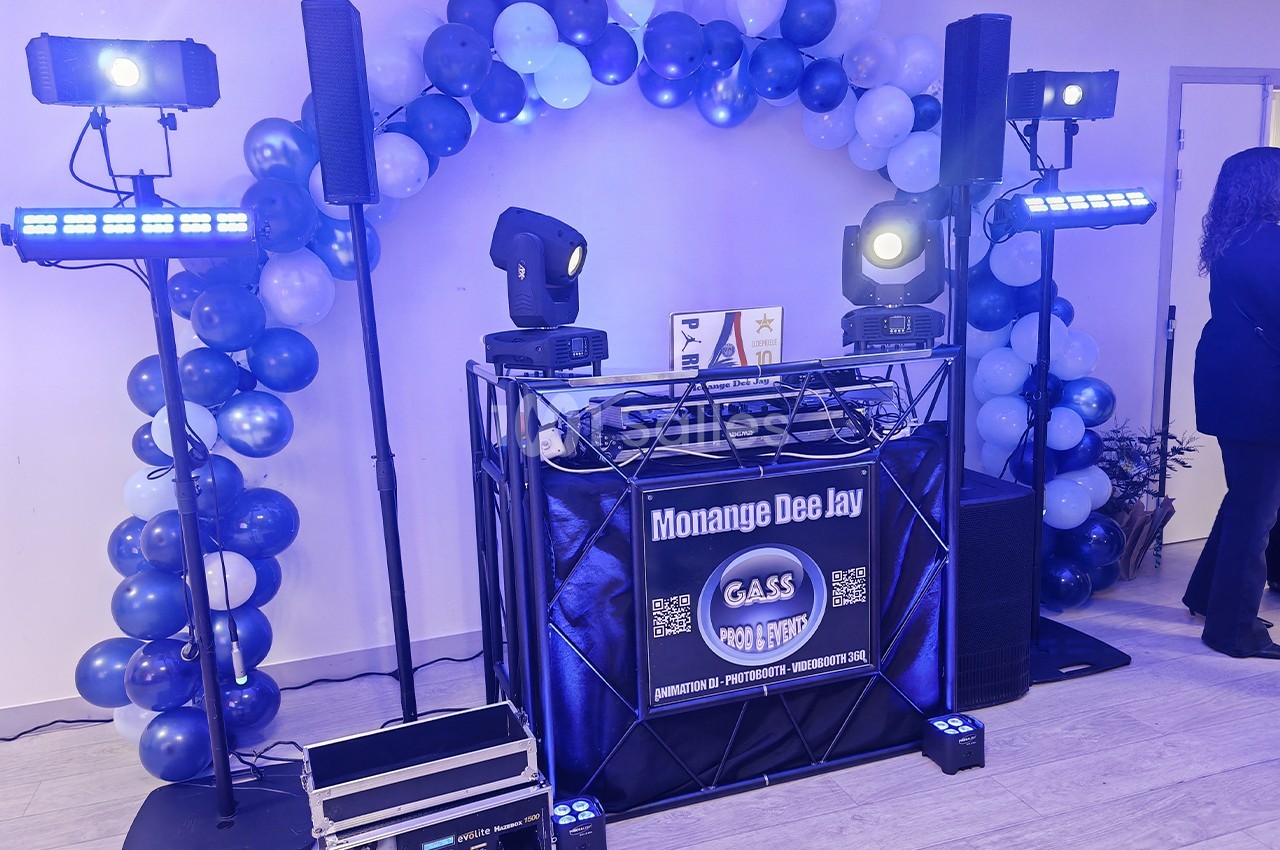 Console de DJ entourée de ballons bleus et blancs, éclairée par des projecteurs dans une salle.