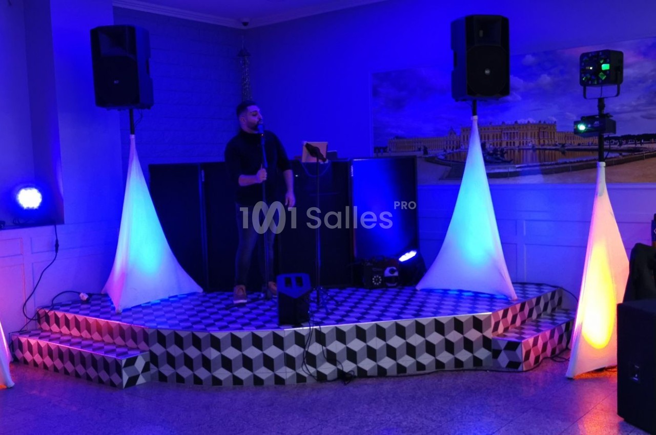 Un homme chante sur une petite scène éclairée par des lumières colorées dans une salle de réception.