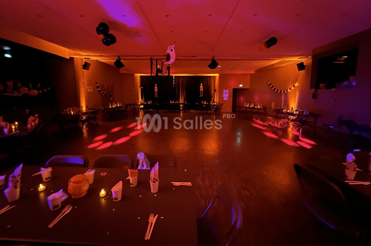 Salle décorée pour une fête, éclairée par des lumières tamisées et ornée de décorations festives sur les tables et murs.